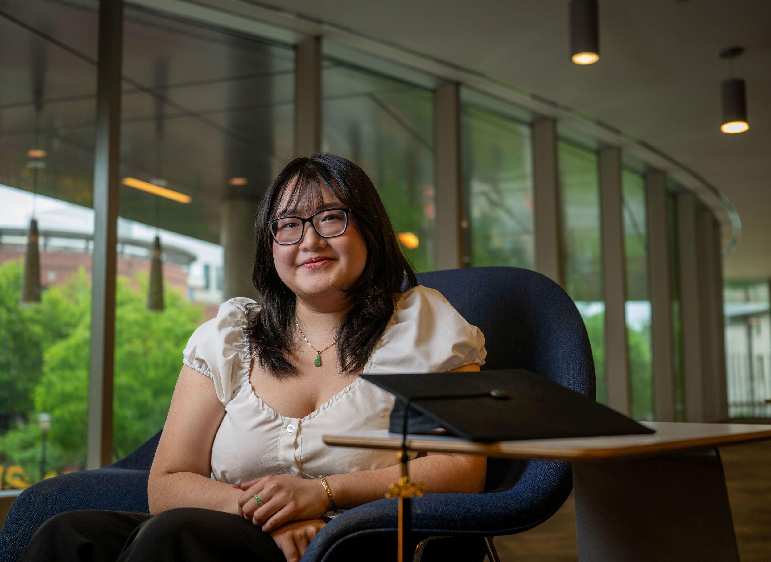 A woman in glasses sits in a blue chair.