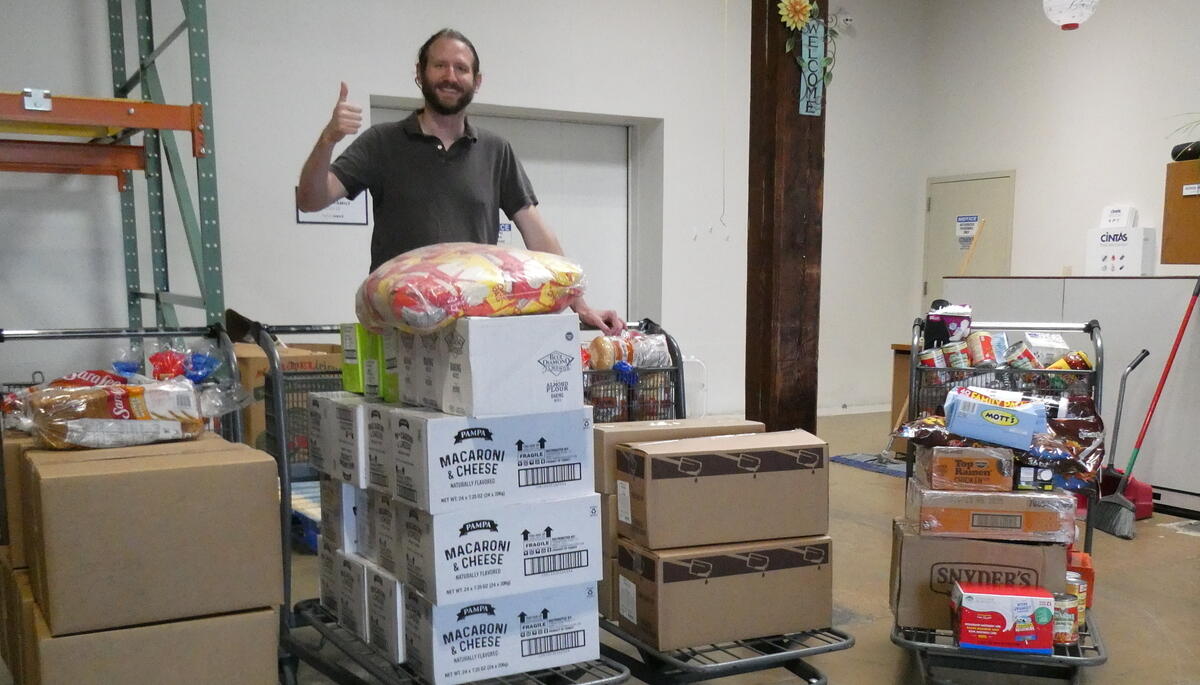 A man standing behind four trollies filled with boxes of food. 