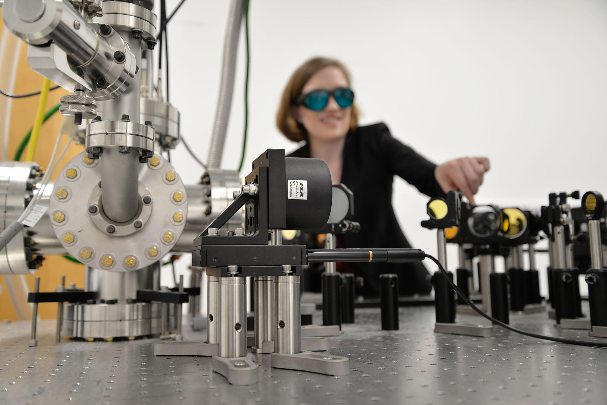 A woman in goggles adjusts a set of mirrors and lab equipment.