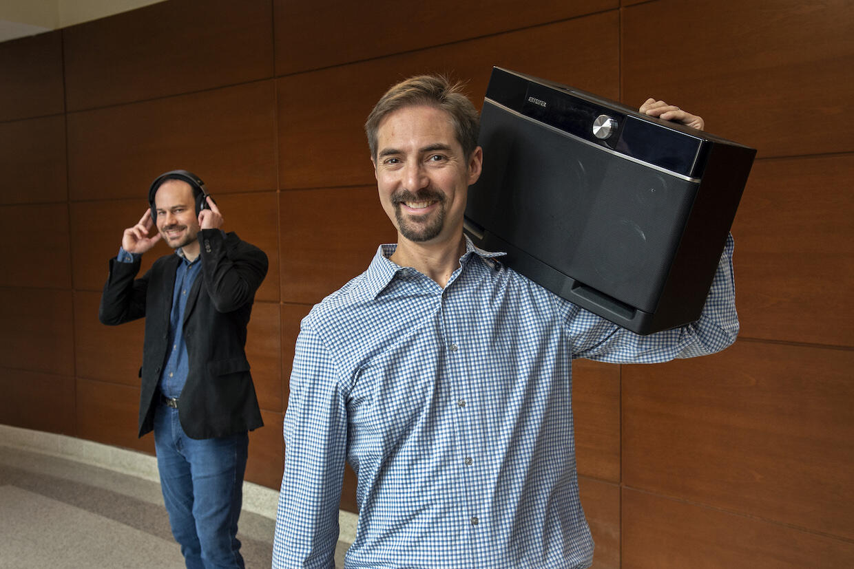 David Shepherd and Douglas Krug. Shepherd is holding a boombox to his ear and Krug is wearing headphones.