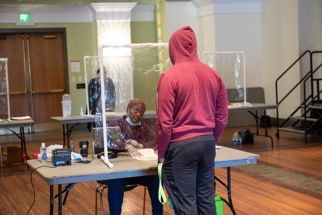 A poll worker sitting behind a protective barrier helps a student voter on election day.