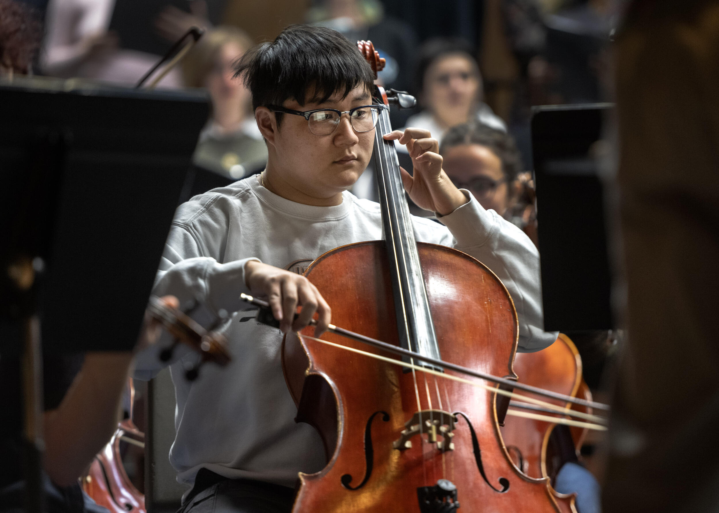 A photo of a man from the waist up. He is sitting and playing the cello. 