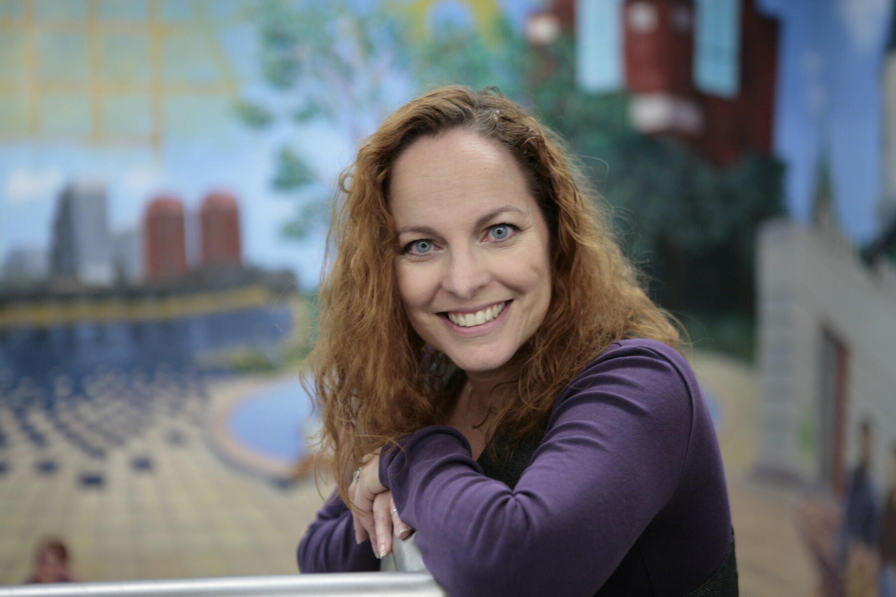 Woman smiling in front of a mural.