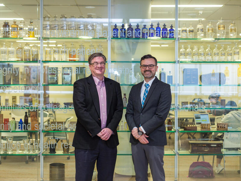 Two people in business suits standing in front of a glass wall.