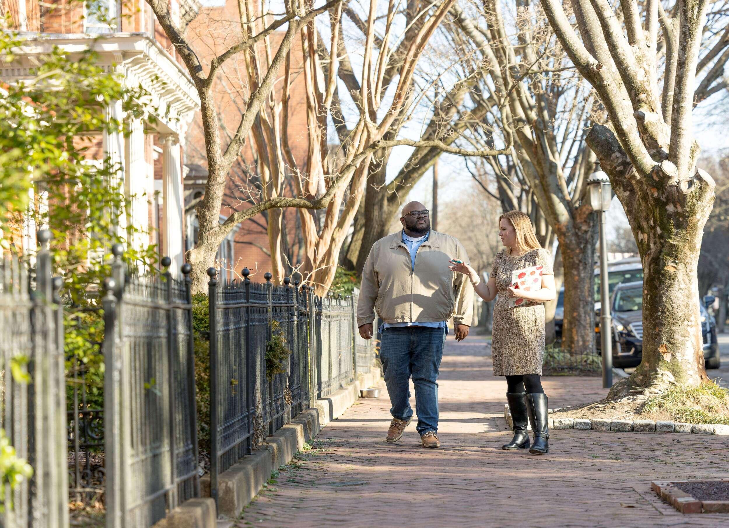 Two people talk while walking down a sidewalk.