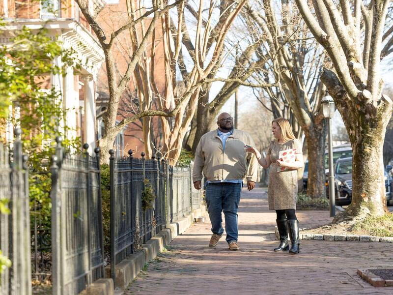 Two people talk while walking down a sidewalk.
