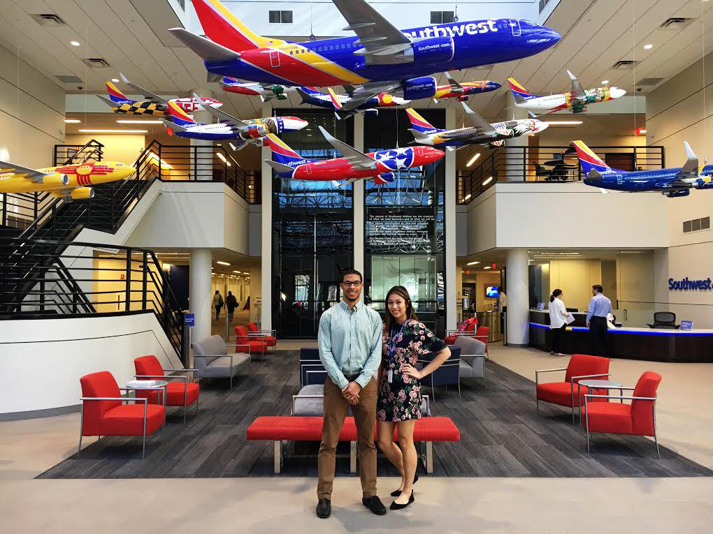 Two people pose in a large room with various model aircraft hanging from the ceiling.