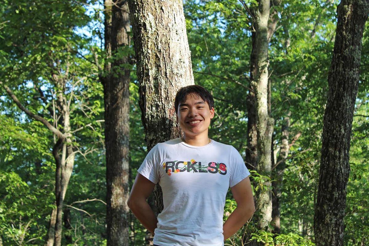 Man stands in front of a tree in a T-shirt and smiles.