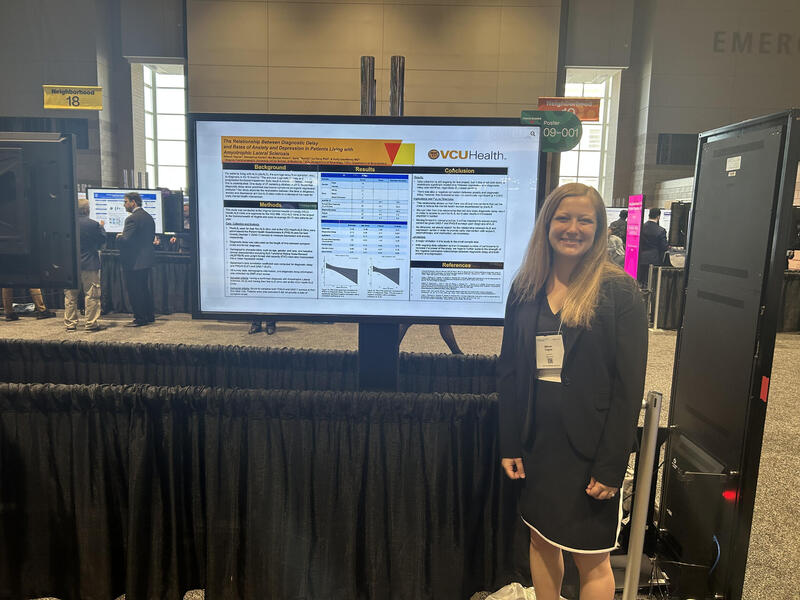 A photo of a woman standing next to a screen displaying her research. 