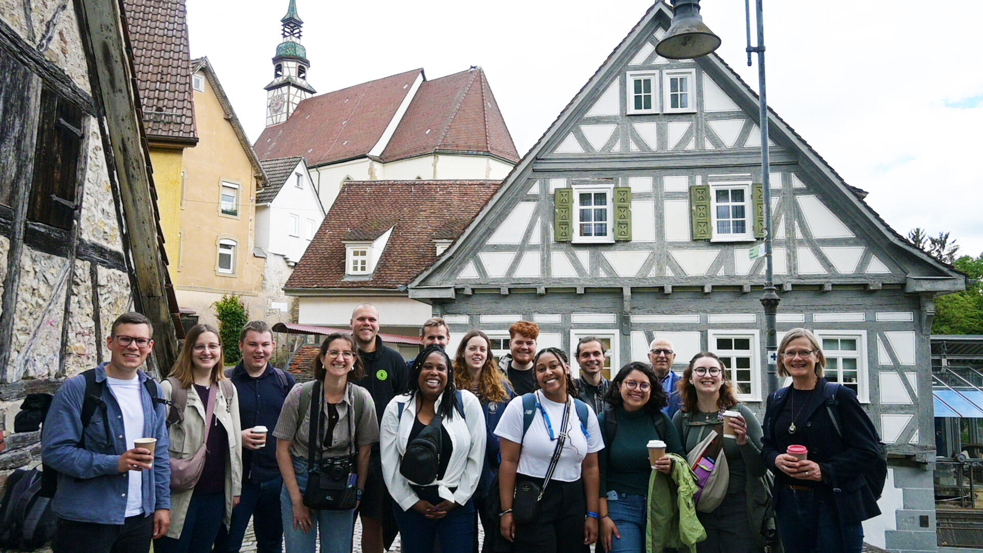 A group photo of 15 people standing in front of historic German buildings. 
