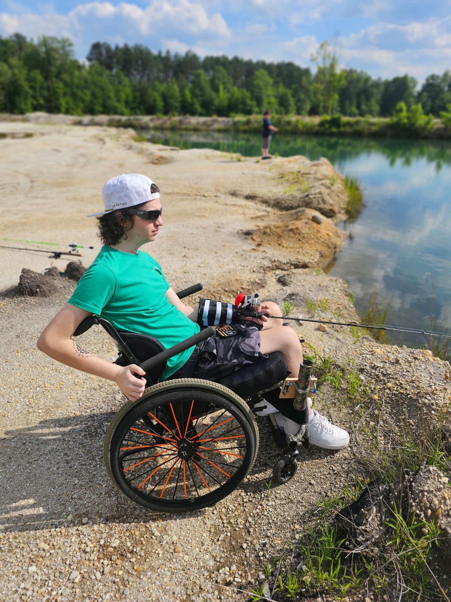 A man in wheelchair fishes alongside a pond.