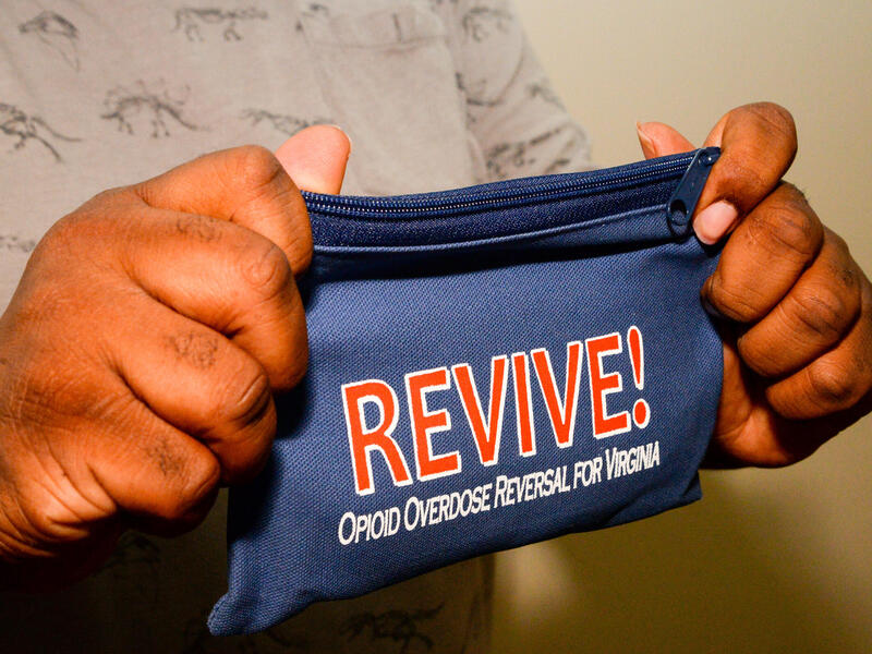 A man holds a small blue zipper bag labelled REVIVE - opioid overdose reversal for Virginia