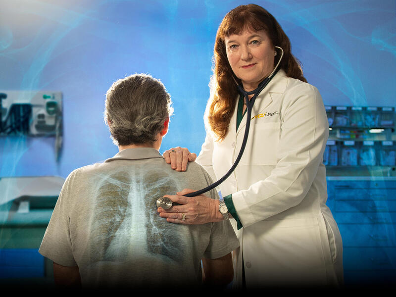 A photo of a woman using a stethoscope on a man's back in a doctor's examination room.