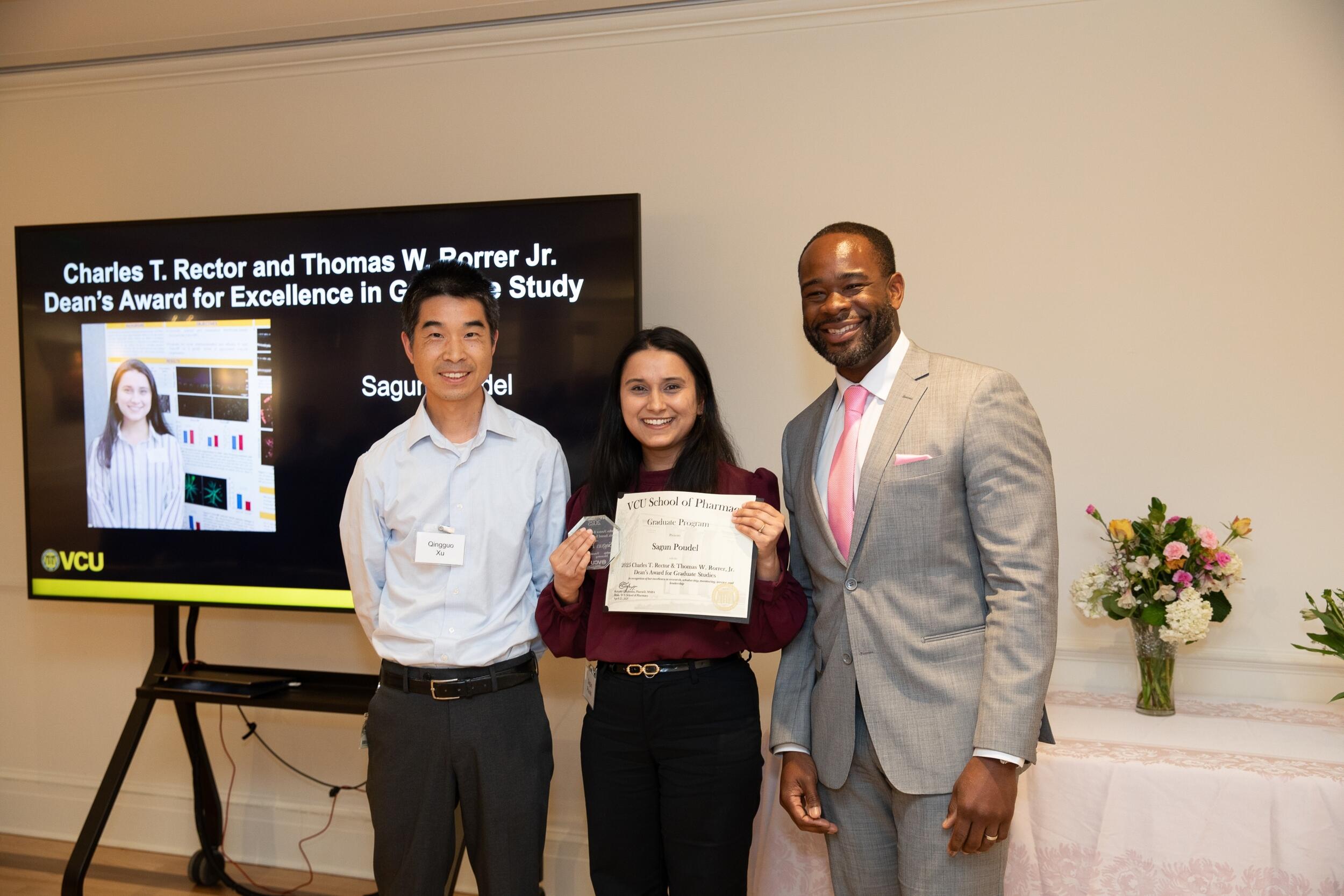 A group photo of three people standing. The woman standing in the middle is holding a certificate. 