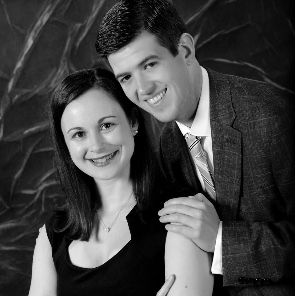 A smiling woman and man. The man leans over the woman's left shoulder.