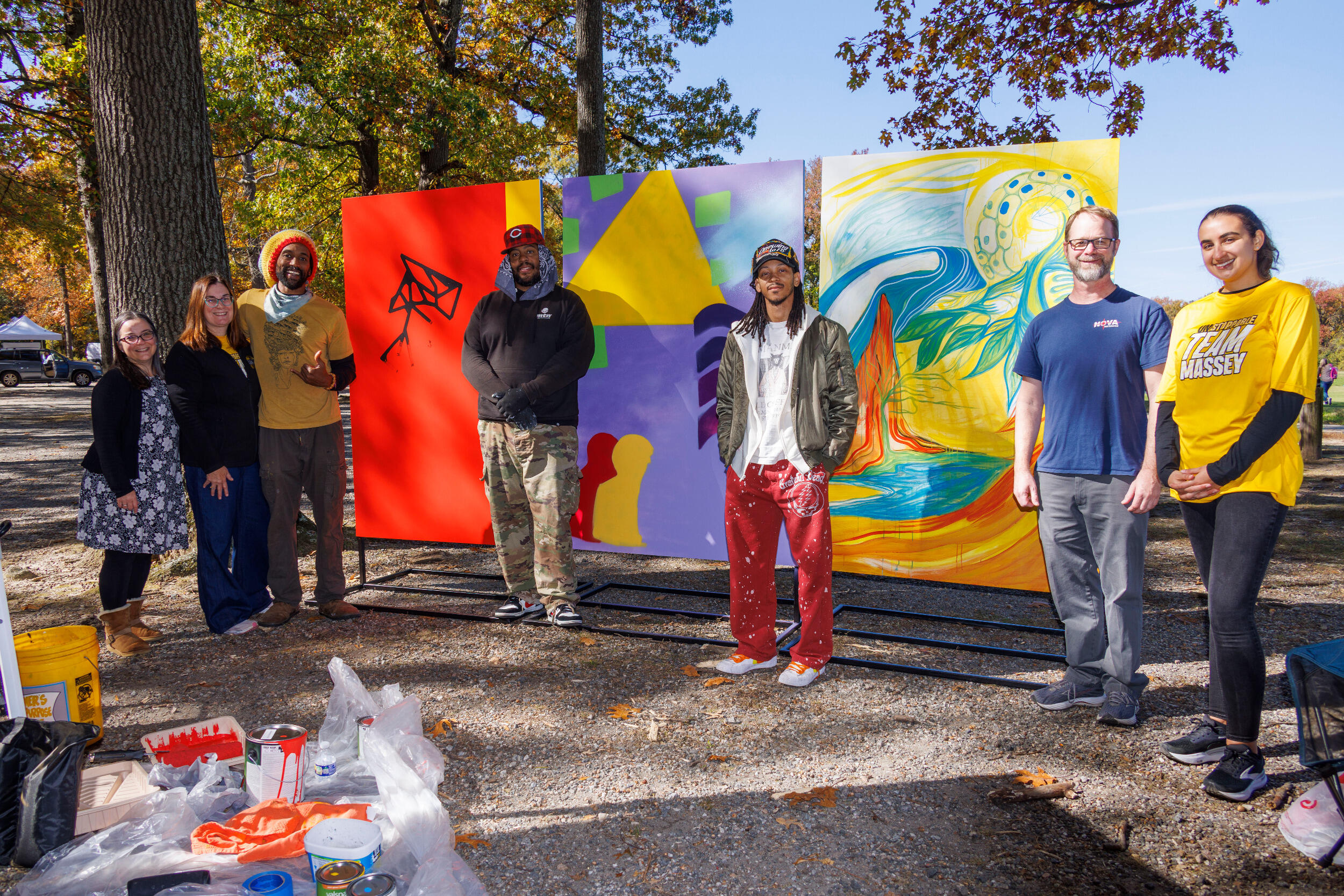 A group of women and men stand in front of a colorful mural.