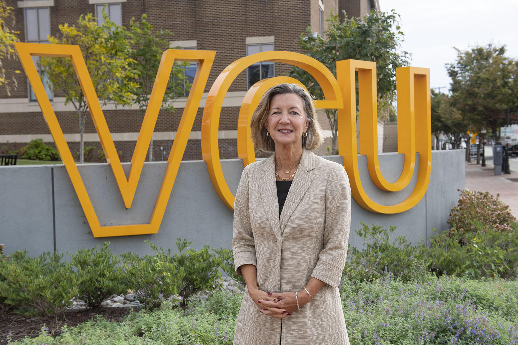 A photo of a woman from the hips up standing in front of a sign with giant yellow letters that spell out \"VCU\"