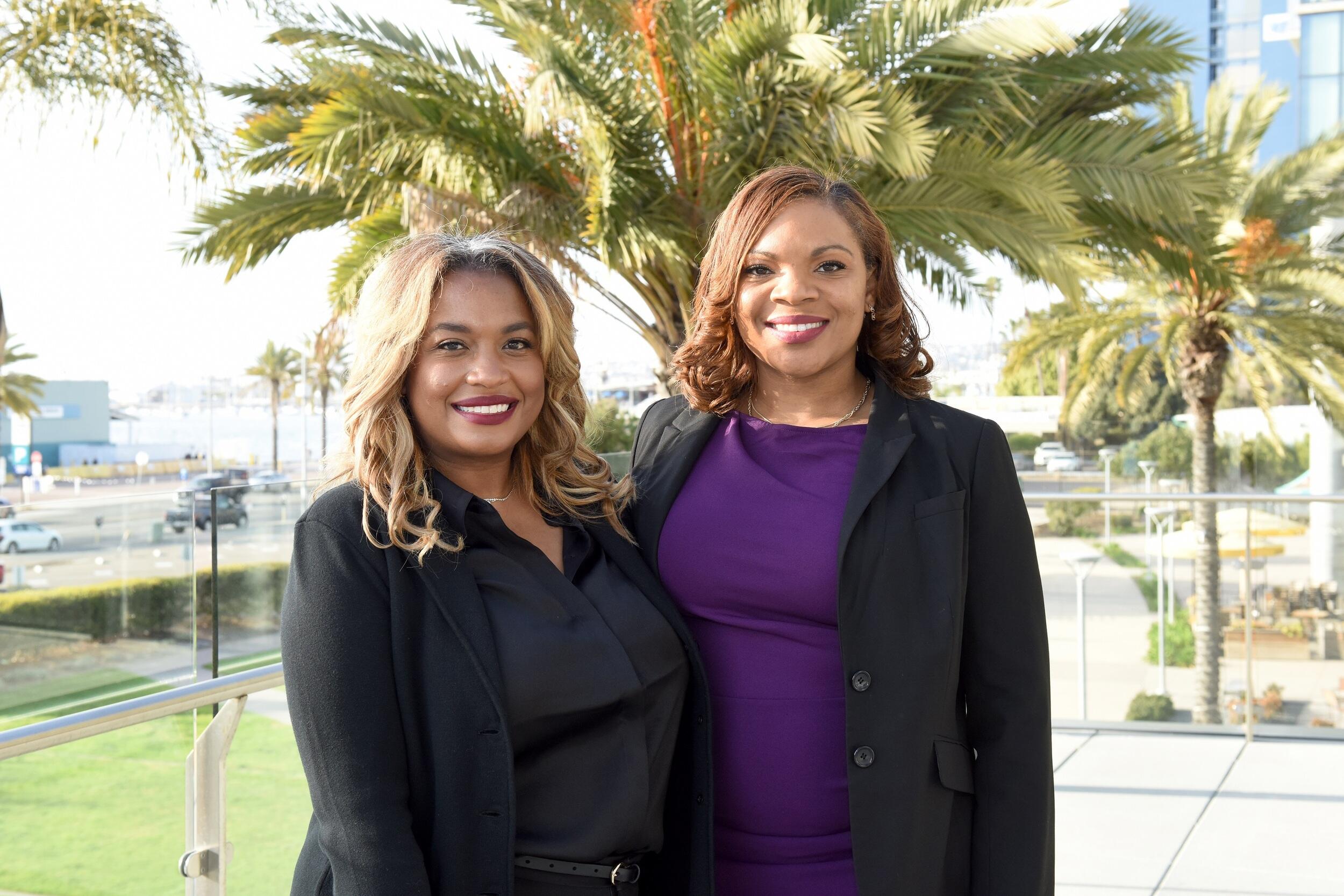 Two women standing next to each other in front of palm trees