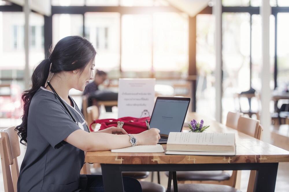 Woman in medical scrubs on laptop computer, in library. 