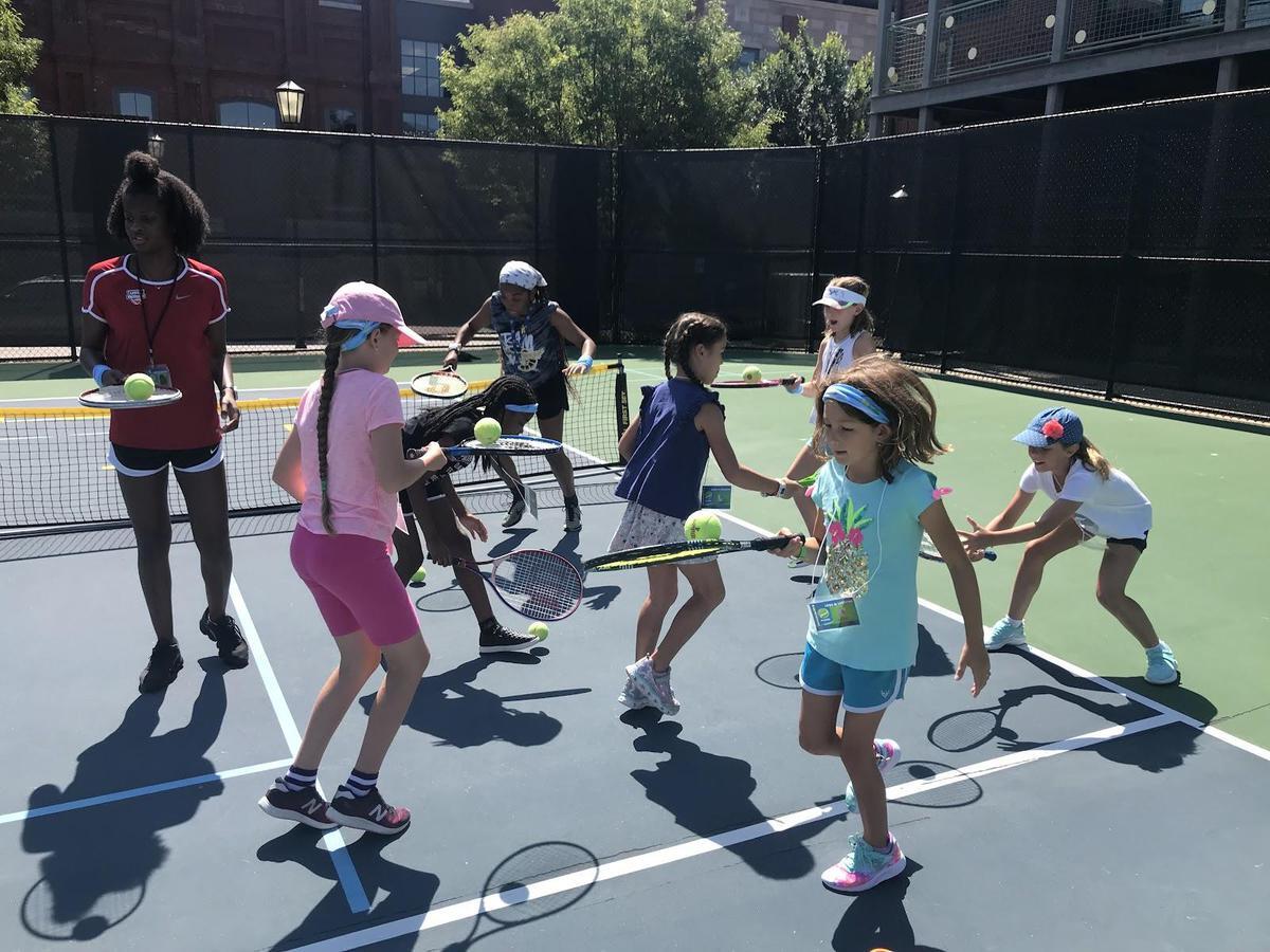 A group of children bouncing balls on tennis rackets on a tennis court. 