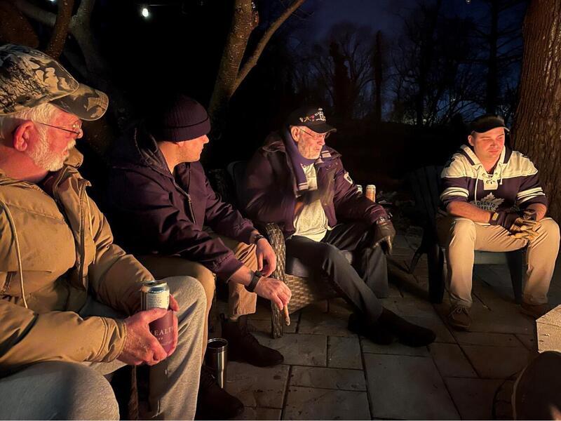 A photo of four men sitting in a semi-circle in the dark. A light from the center of the circle is illuminating them. 