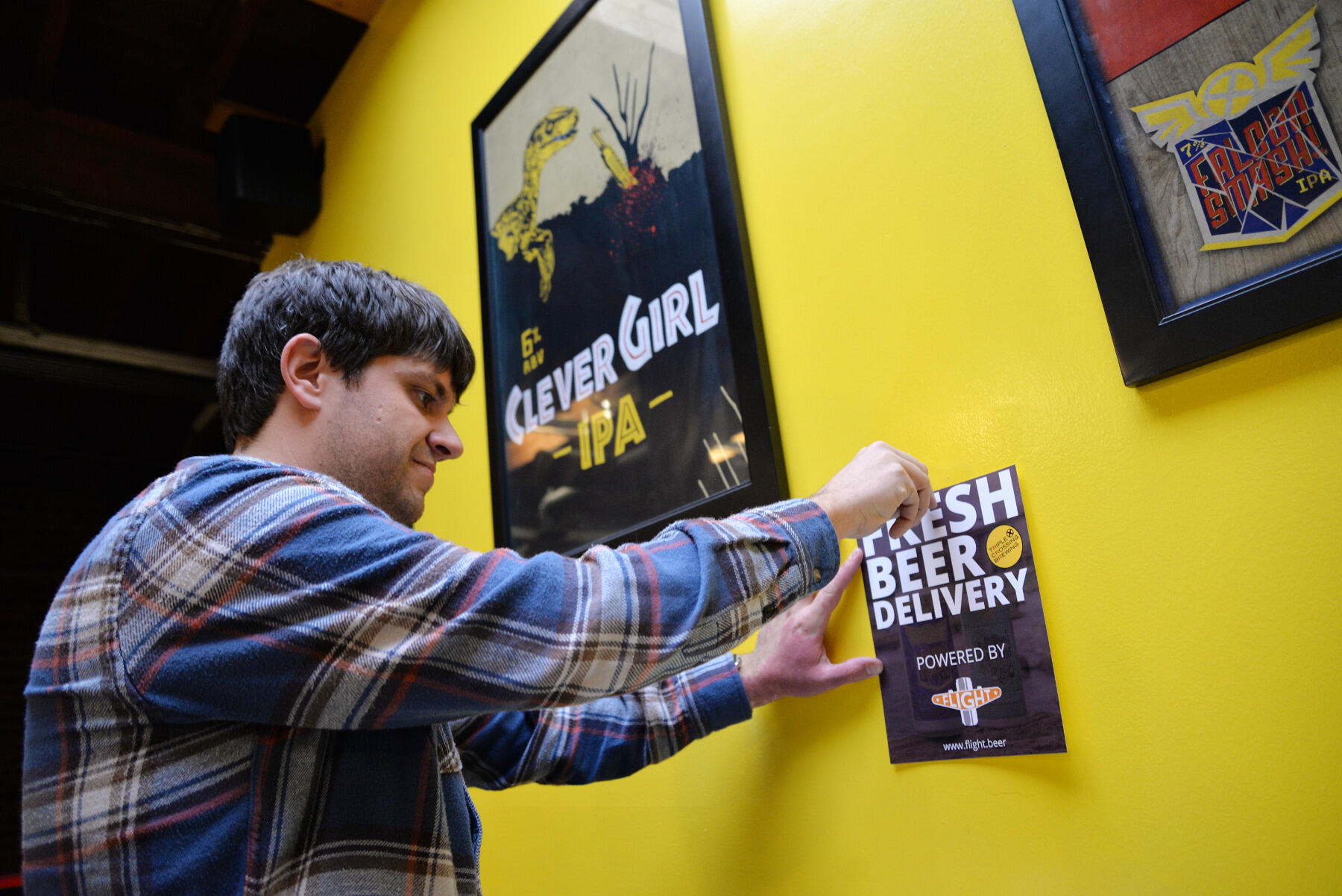 At Triple Crossing Brewing, Flight co-founder Matthew Teachey tapes up a flyer about his craft beer delivery service, seeking to raise awareness among Richmond craft beer fans.