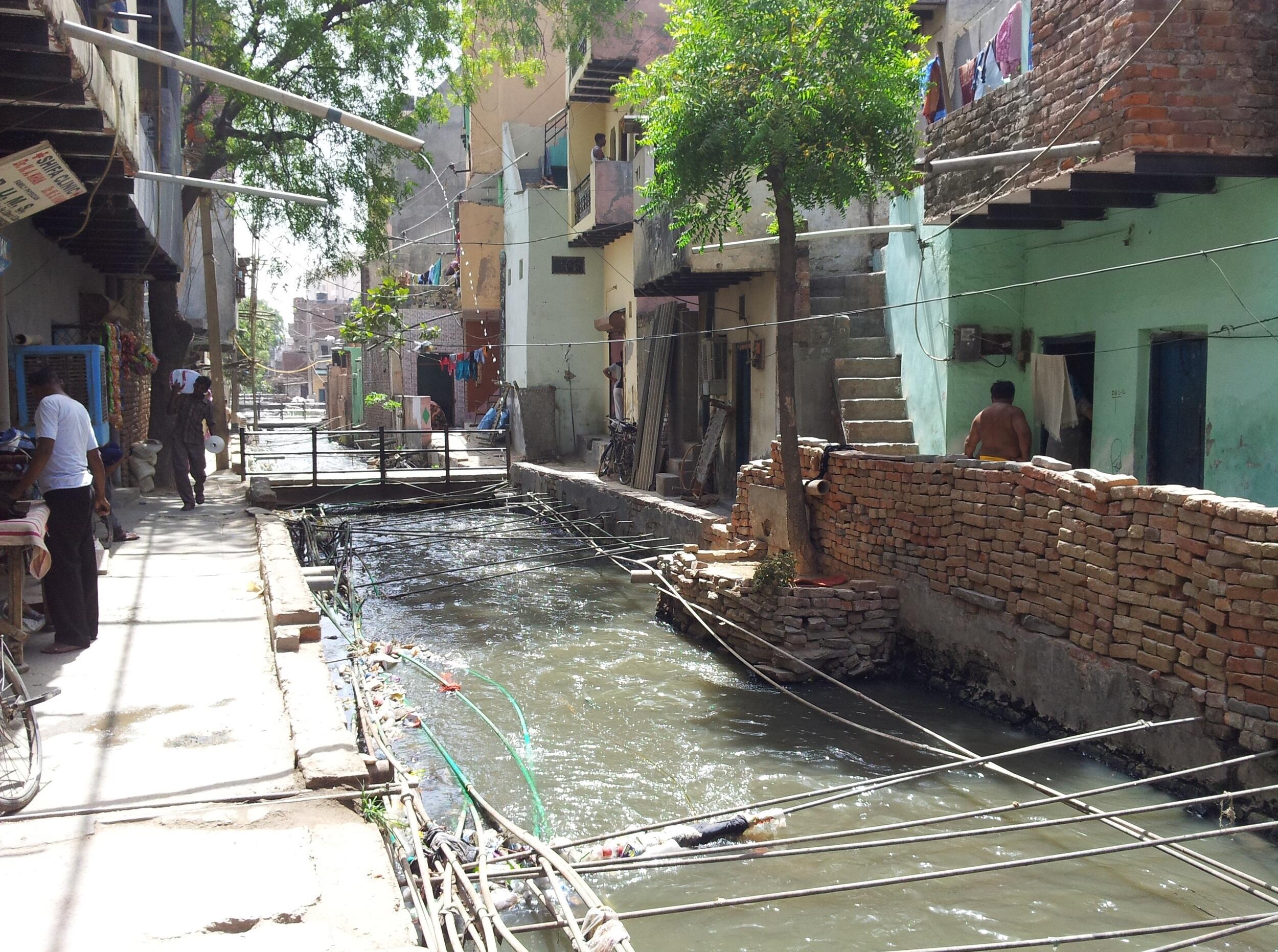 An improvised drain with sidewalks on both sides and trees hanging over it in India.