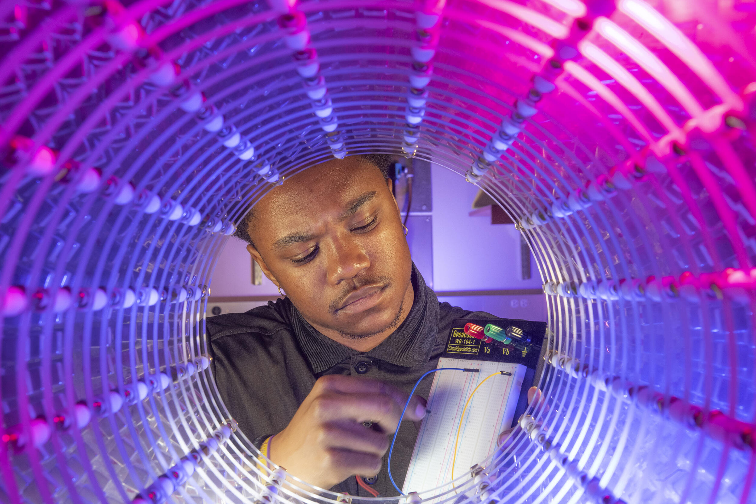 A photo of a man plugging a wire into a device at the end of a blue and pink tunnel. 