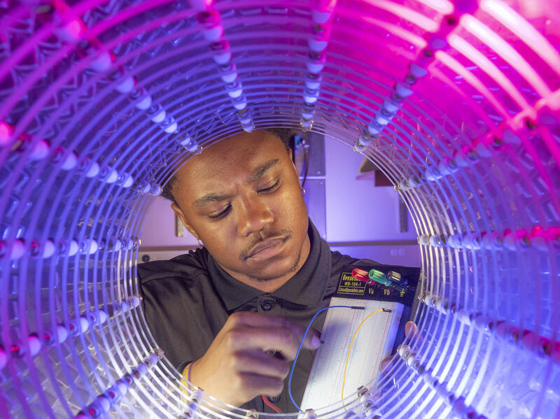 A photo of a man plugging a wire into a device at the end of a blue and pink tunnel. 