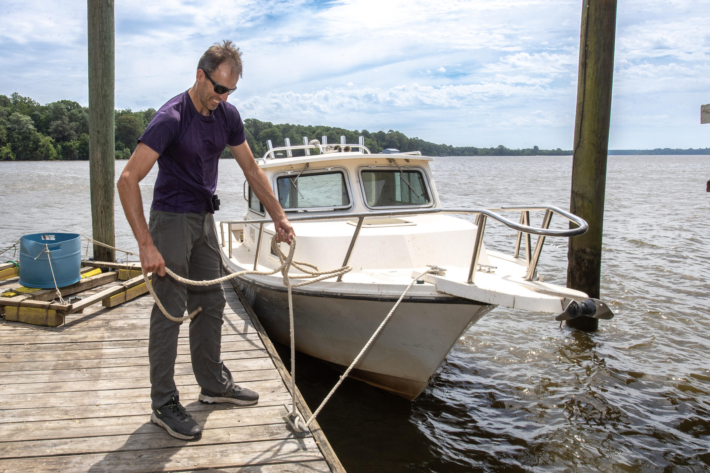 A photo on a boat dock holding onto a rope that is attached to a white boat. 