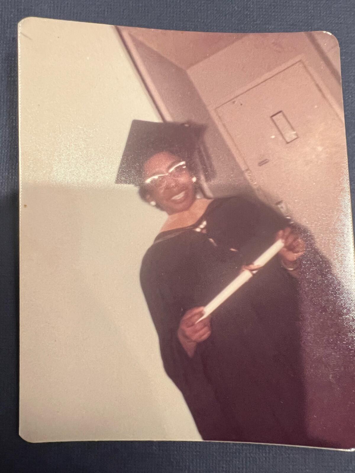 An old photo of a woman wearng a graduation cap and gown while holding a rolled up certificate. 
