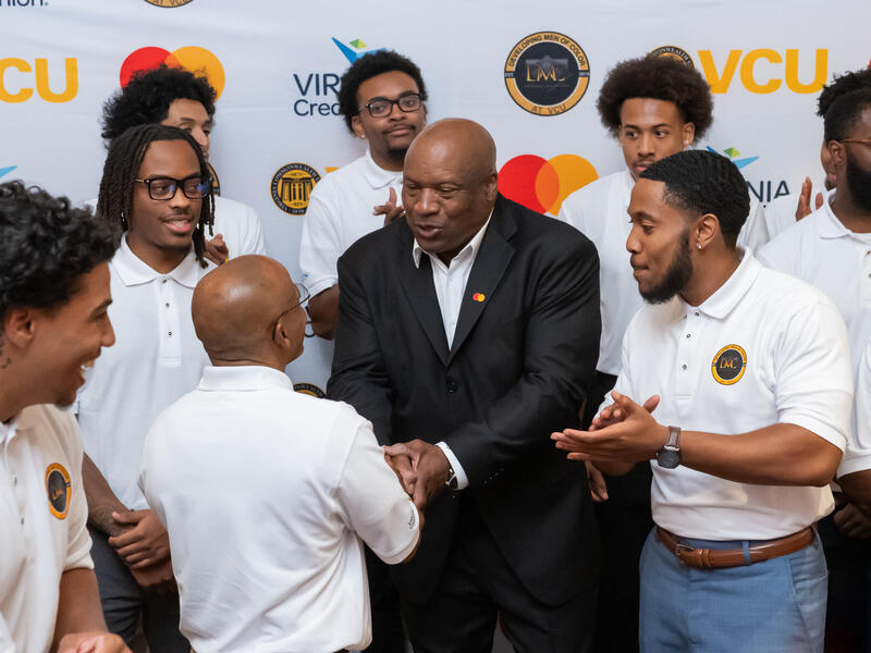 Bo Jackson, wearing a suit, shakes hands with a man in a white shirt and is surrounded by other men in white shirts.