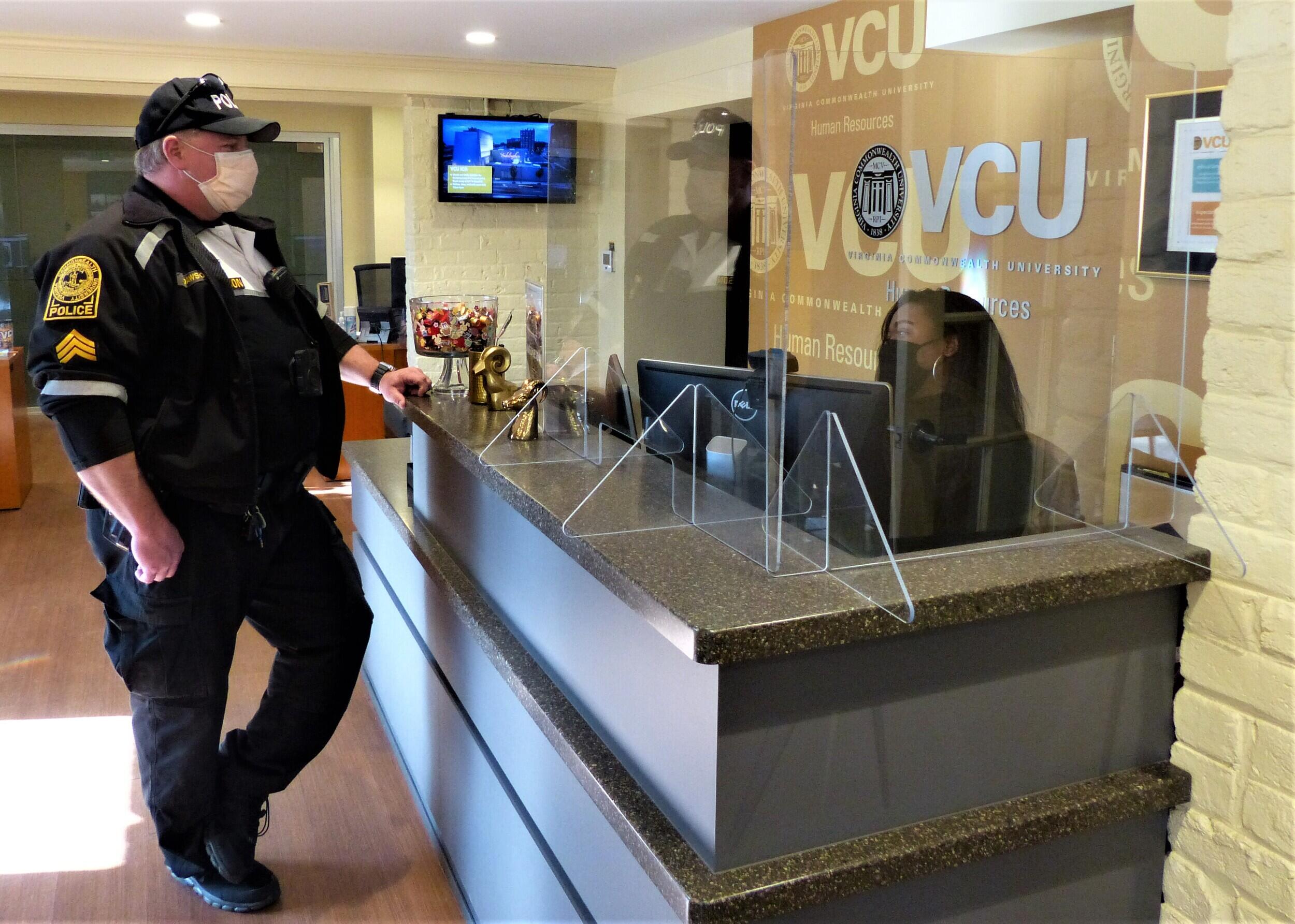 VCU police officer stands in front of reception desk speaking with woman sitting at the desk.
