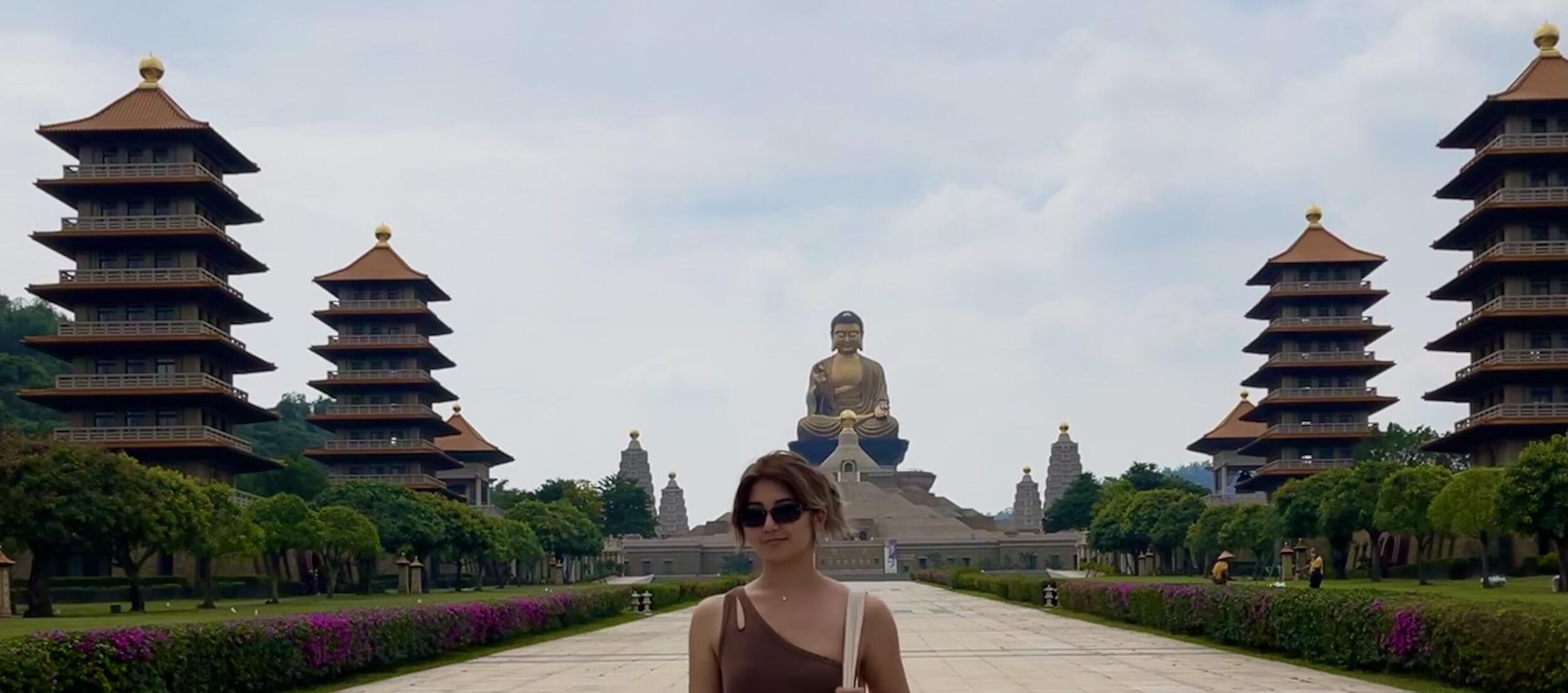 Naomi Ghahrai standing in the foreground on a pathway that leads to a large Buddhist monastery.