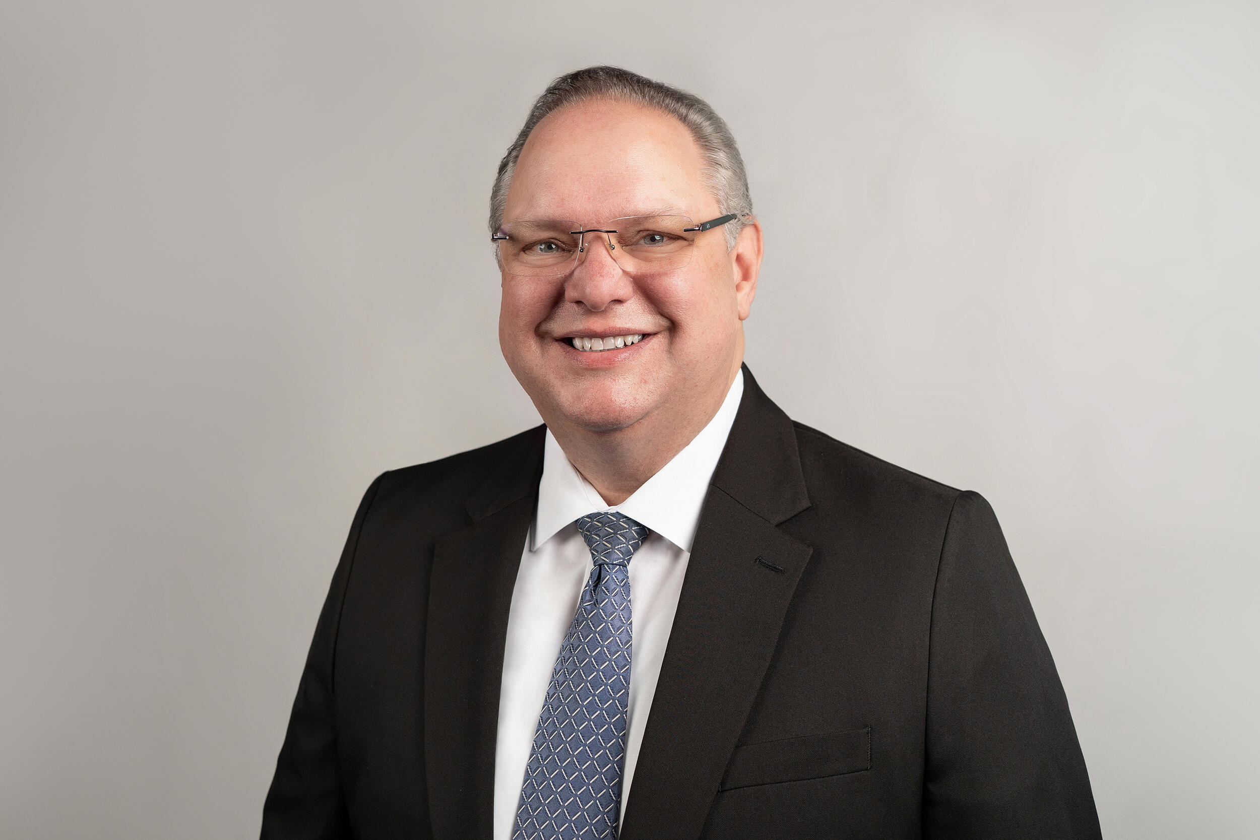 A man wearing glasses and a coat and tie, smiling.