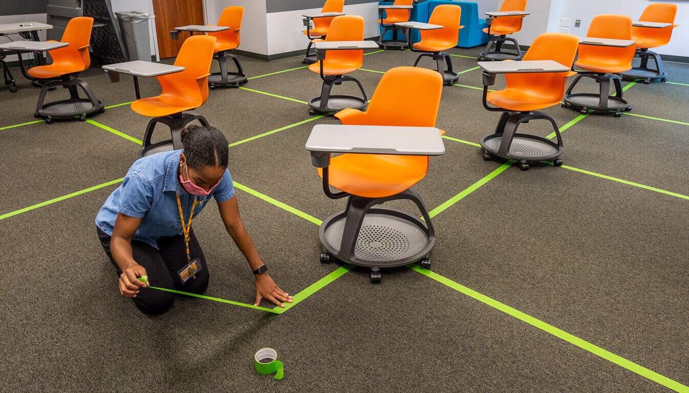 A VCU employee measures the distance between chairs in a classroom