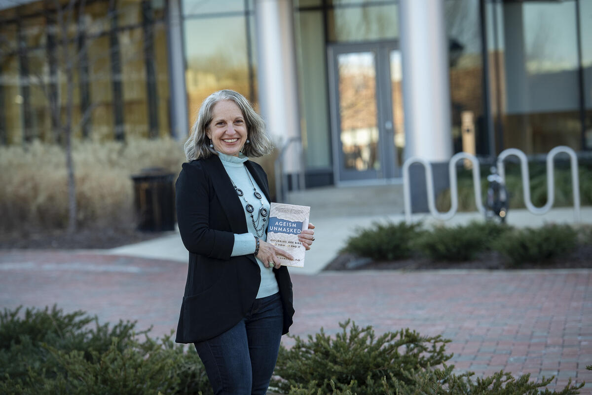 Tracey Gendron, Ph.D., director of the Virginia Center on Aging at VCU, holding her new book \"Ageism Unmasked: Exploring Age Bias and How to End It\" in front of Cabell Library 