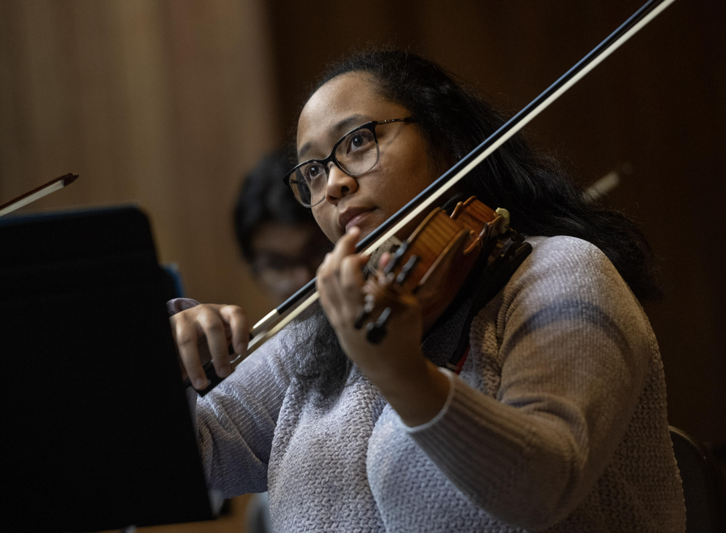 A photo of a woman from the chest up. She is playing a violin. 