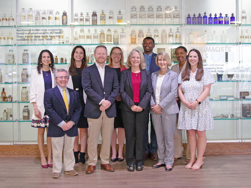 A group photo of ten people standing in front of old apothecary bottles. 