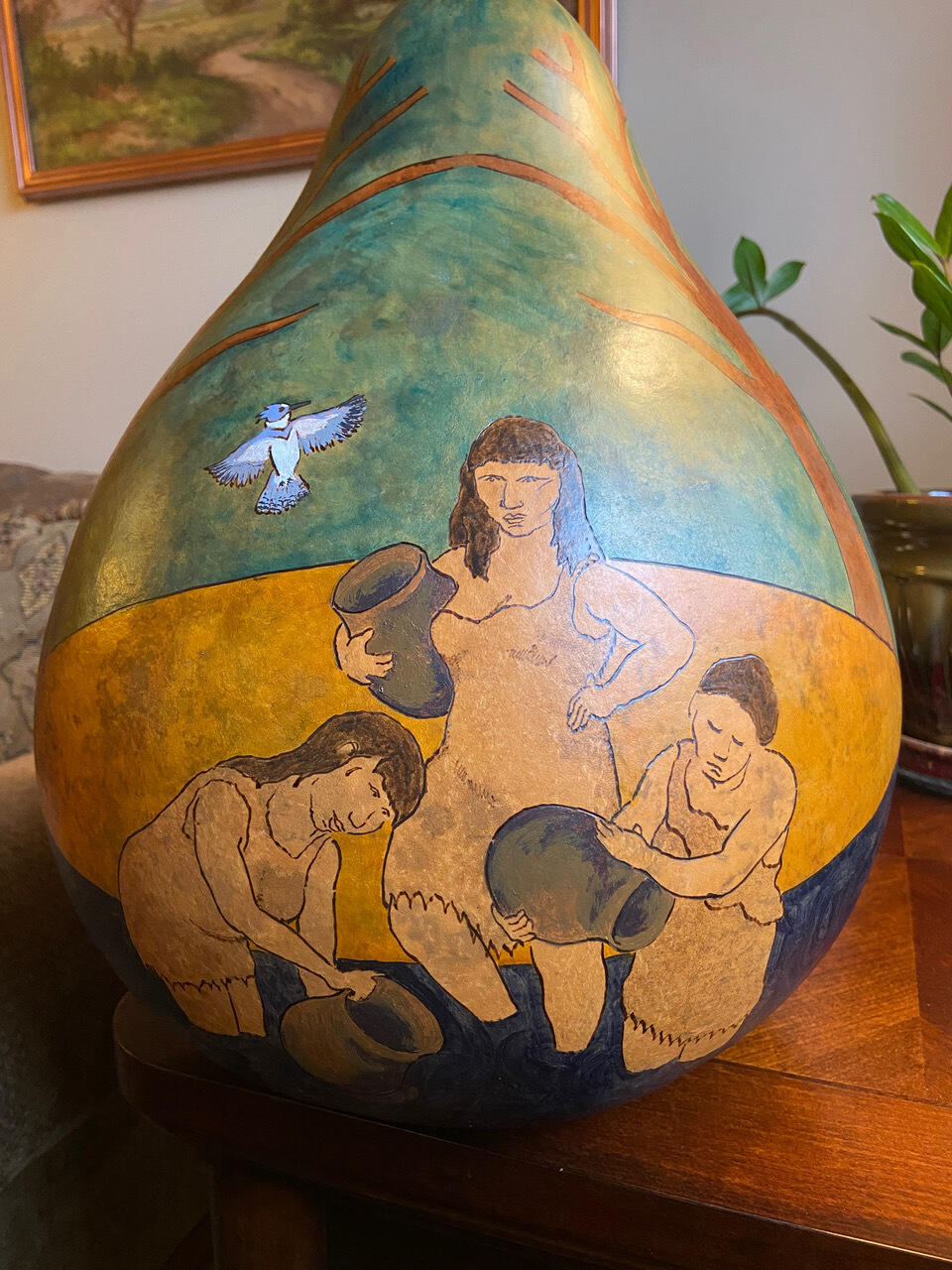 A dried gourd with an image of four women holding bowls standing in water on it. 