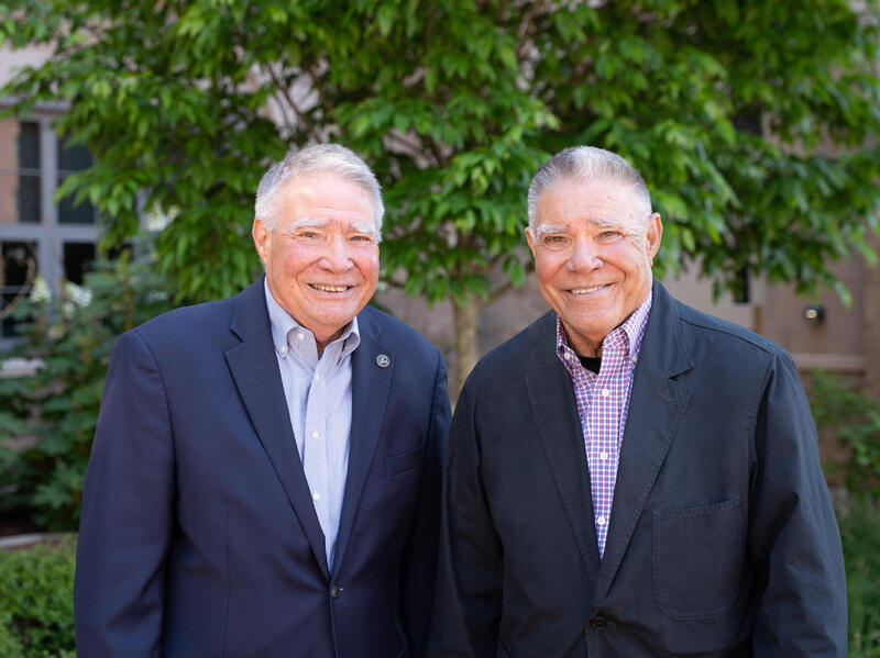 A photo of two men from the chest up who are standing outside an d smiling. 
