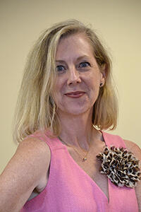 A portrait of Catherine Ingrassia, Ph.D. wearing a pink blouse with a cheetah print flower on it. 