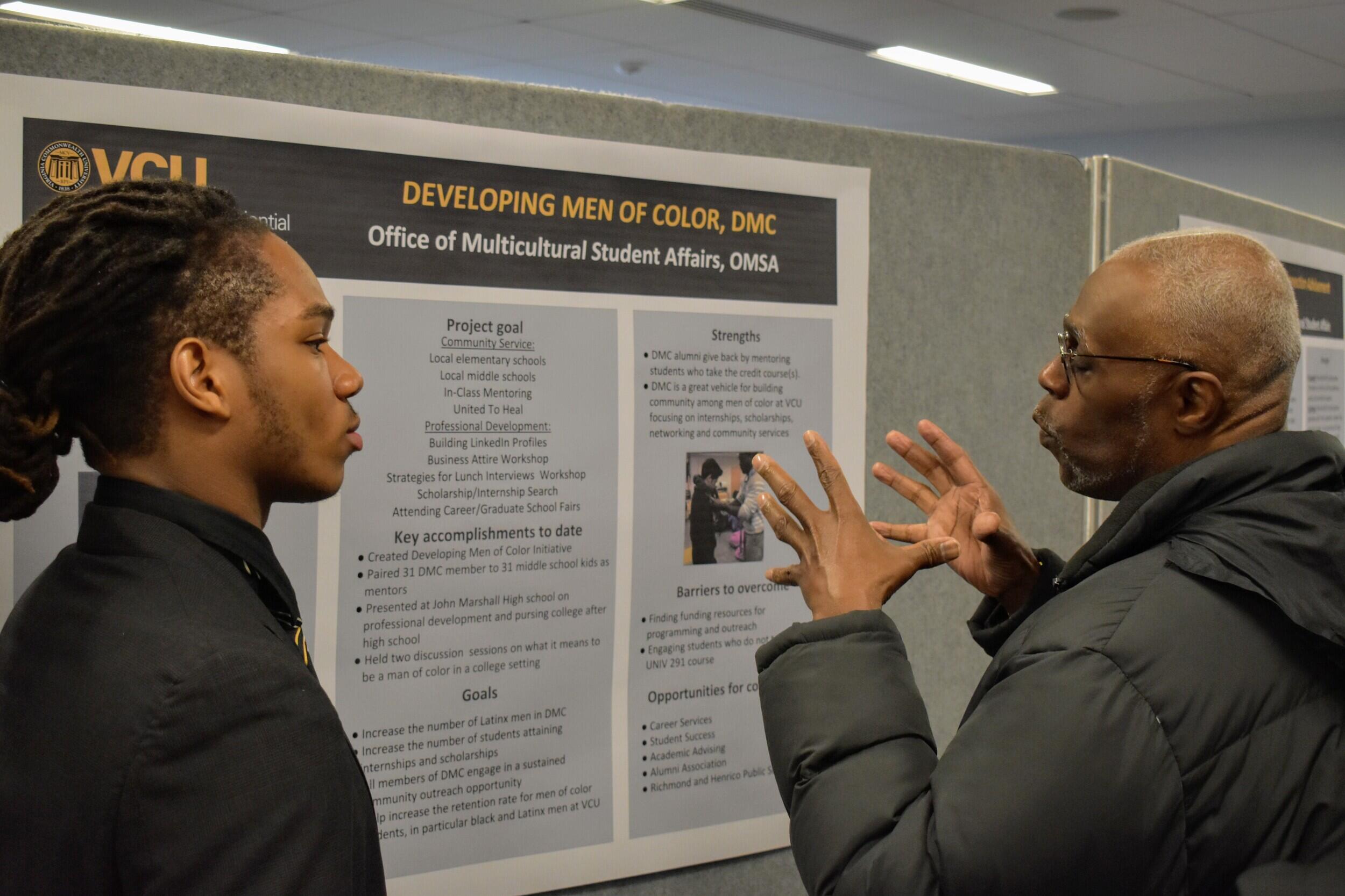 Two people speaking in front of a poster.