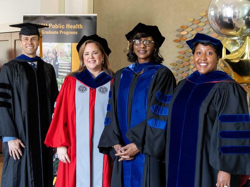 A group photo of four people wearing doctorate graduation cap and gowns. 