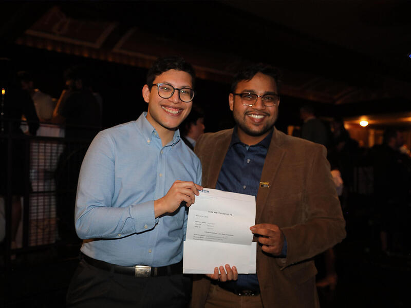 A photo of two men holding a piece of paper and smiling. 