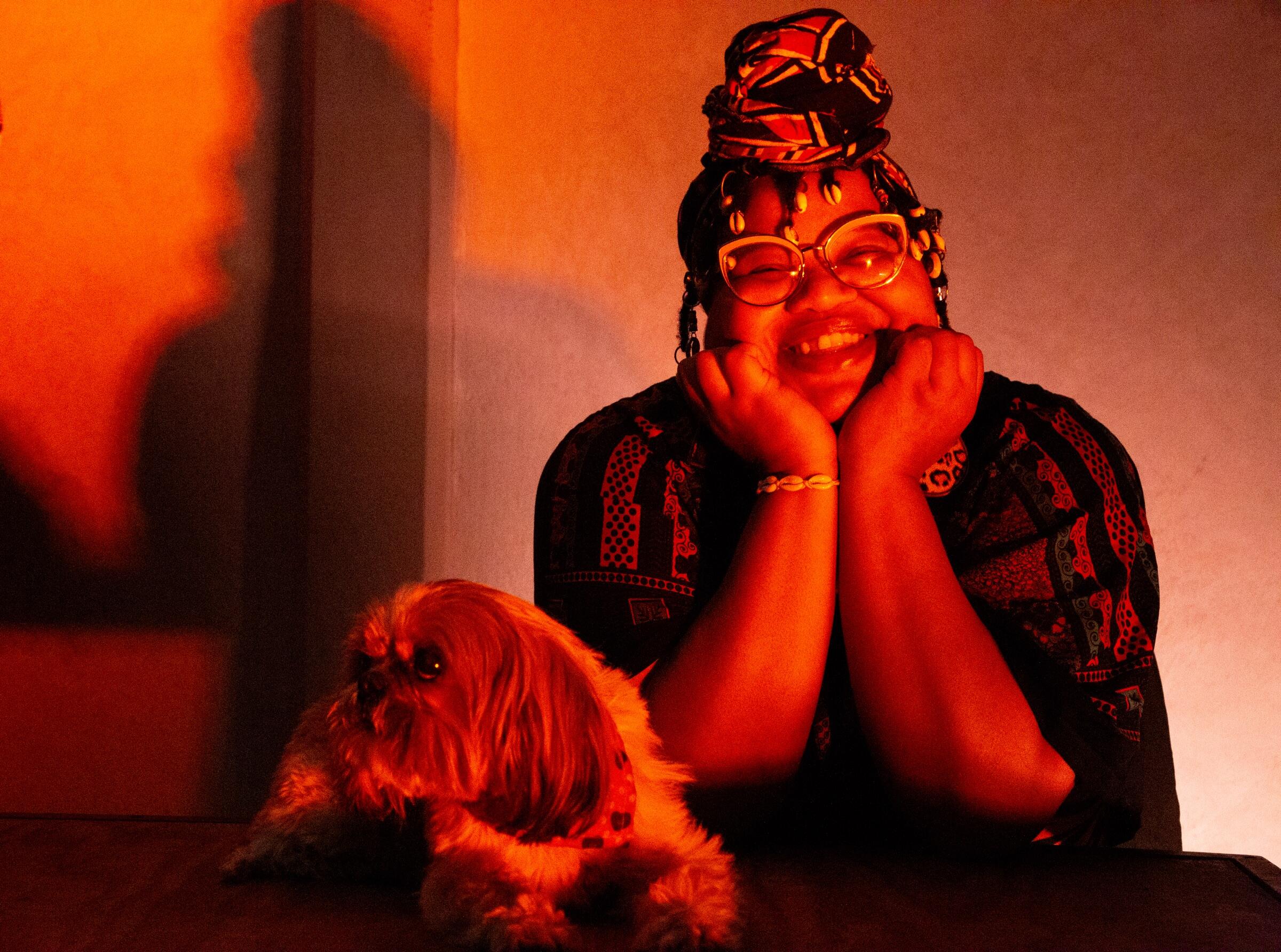 A smiling woman wearing a head scarf and glasses next to a small dog 