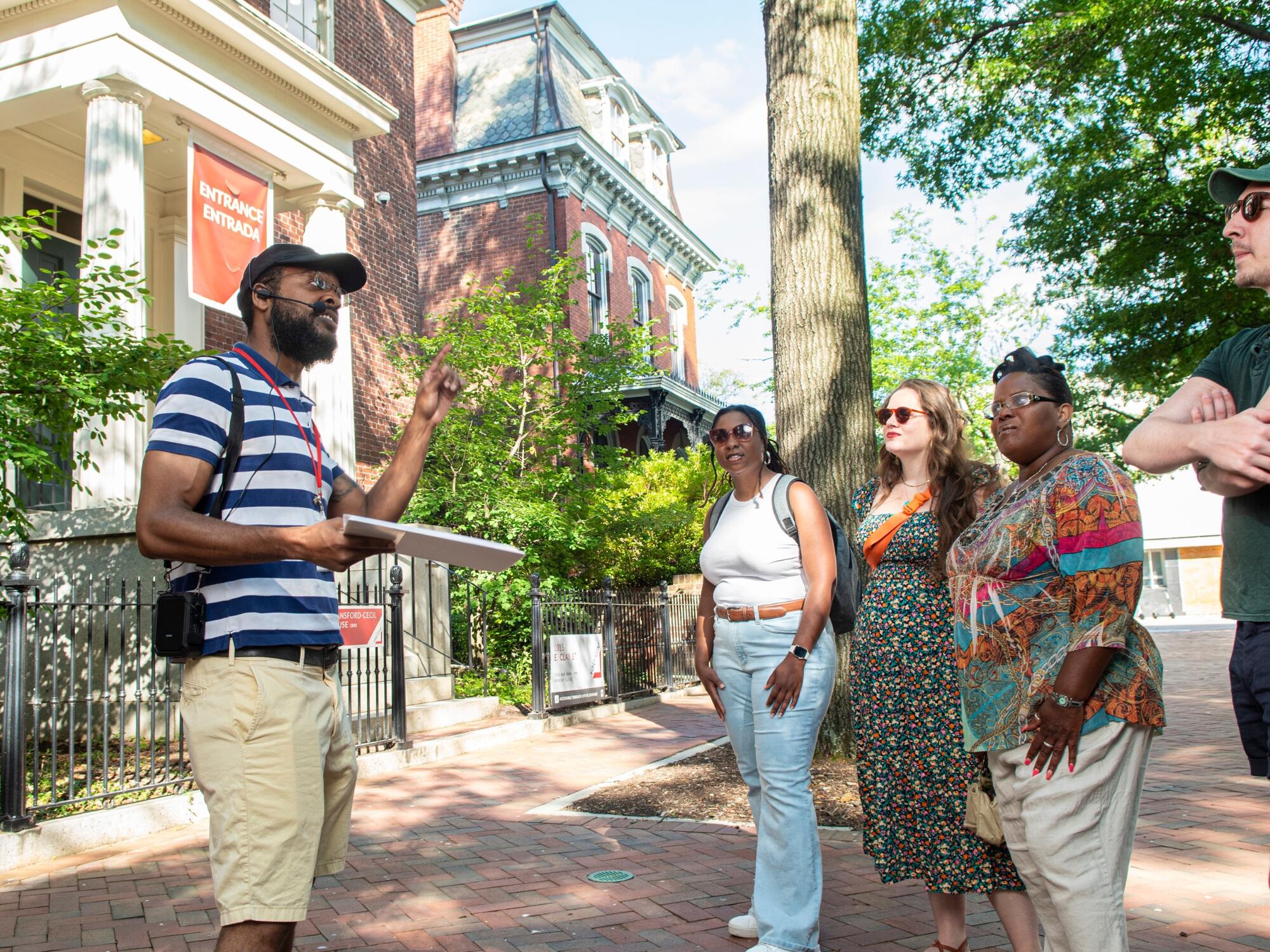 A photo of a man talking to three woman and one other man in front of a historical building. 