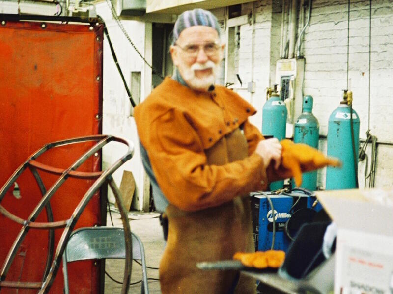 Man in welding clothes stands in a studio.