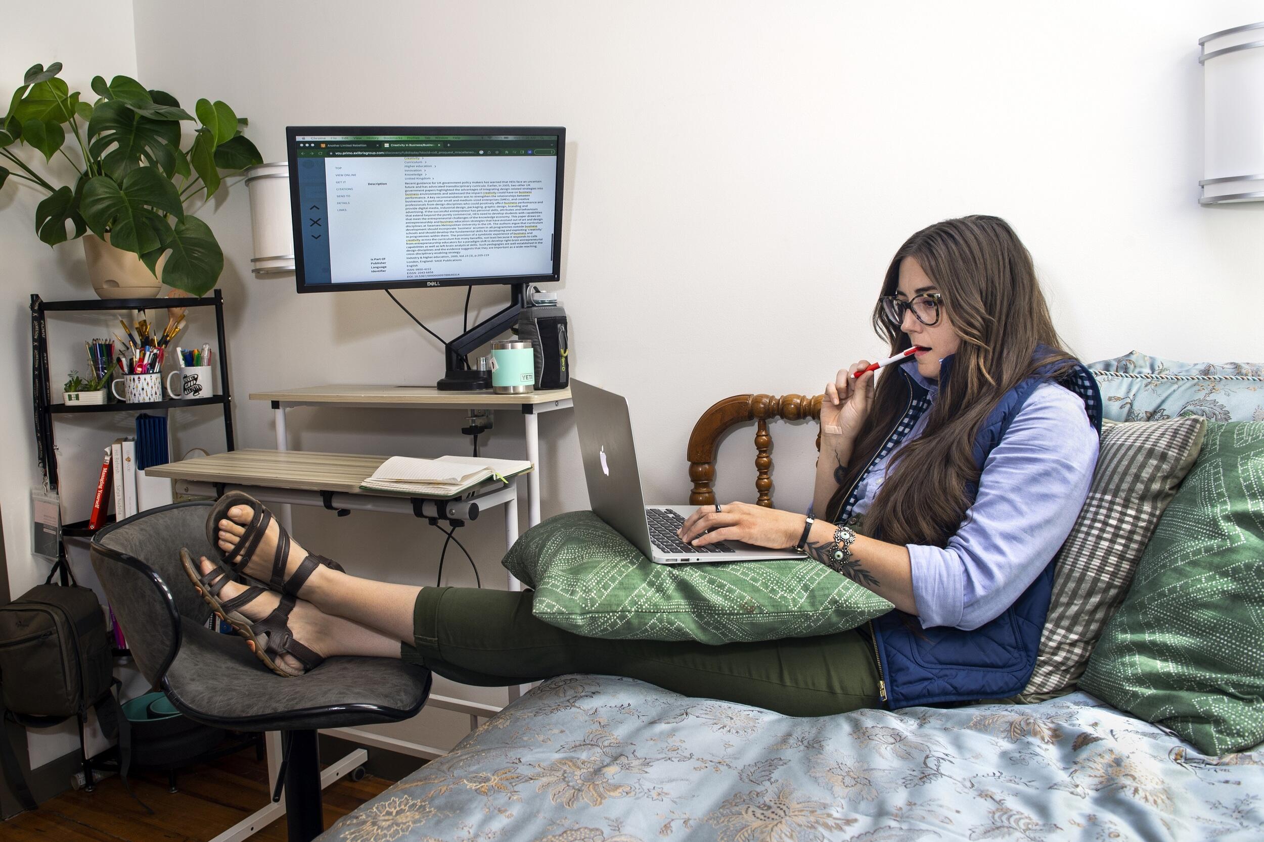 A photo of a woman sitting on a bed with a laptop on her lap. 