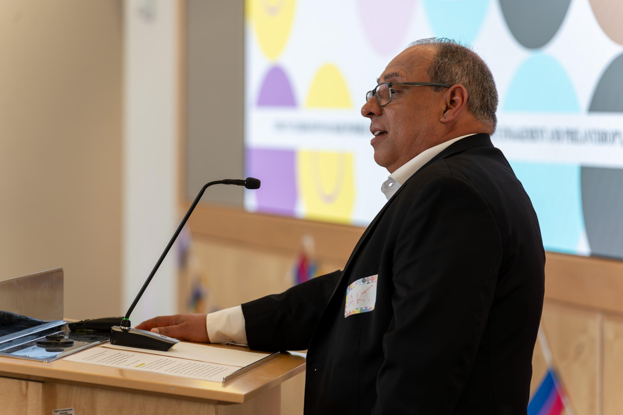 A photo of a man speaking into a microphone from behind a podium. 
